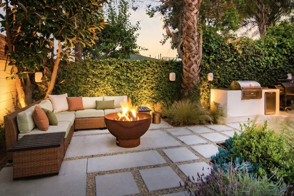 Landscape design and build featuring concrete patio pads with gravel joints, a fire pit seating area, outdoor kitchen grill, planting, and landscape lighting, designed and installed by Lush Gardens Inc.