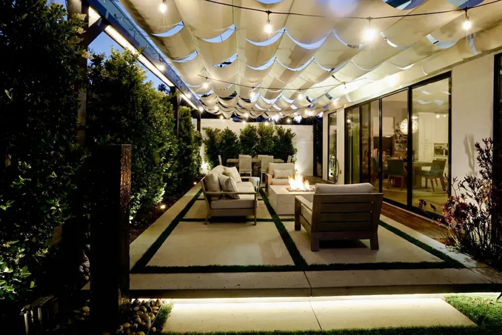 Modern backyard patio with integrated landscape lighting, string lights, illuminated concrete walkways, and a fire feature seating area, designed and installed by Lush Gardens Inc.