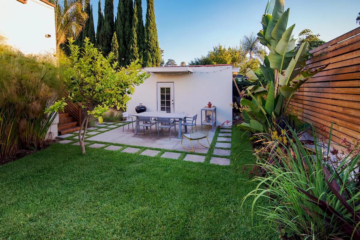 Backyard landscape construction featuring a green lawn, concrete stepping stone patio, layered planting, and a horizontal wood fence