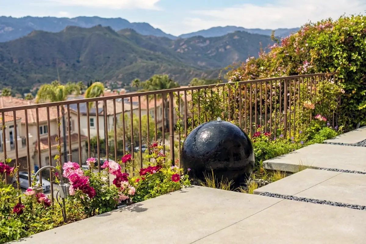 Hillside landscape and softscape featuring flowering planting beds, concrete walkways, and a decorative water feature with mountain views