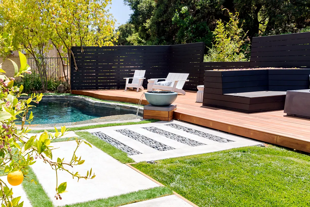 Modern backyard landscape and softscape featuring custom pool, concrete walkways with gravel joints, lawn areas, and wood deck designed and installed by Lush Gardens Inc.