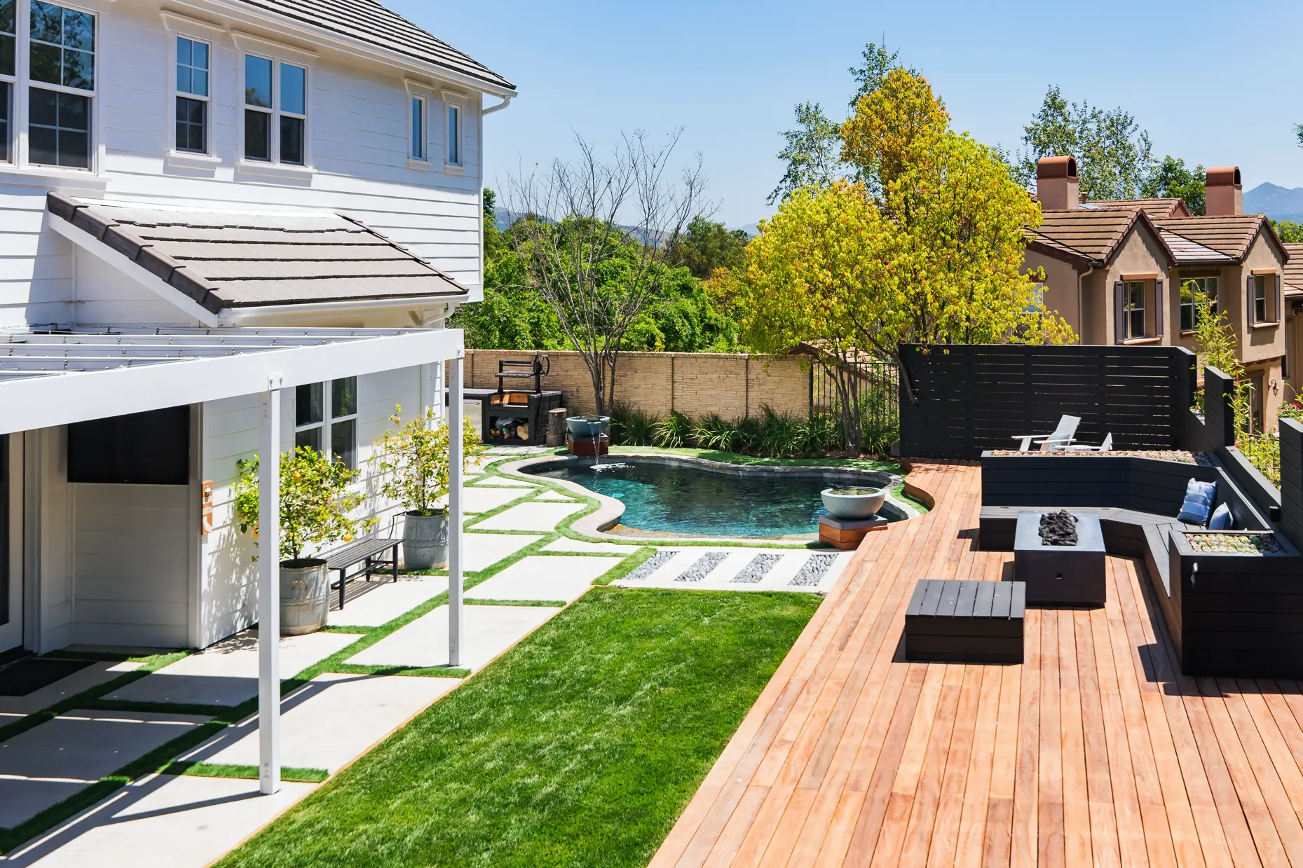 Modern backyard landscape and softscape with custom wood deck, integrated lawn, concrete walkways, pool, privacy fencing, and outdoor seating designed and installed by Lush Gardens Inc.