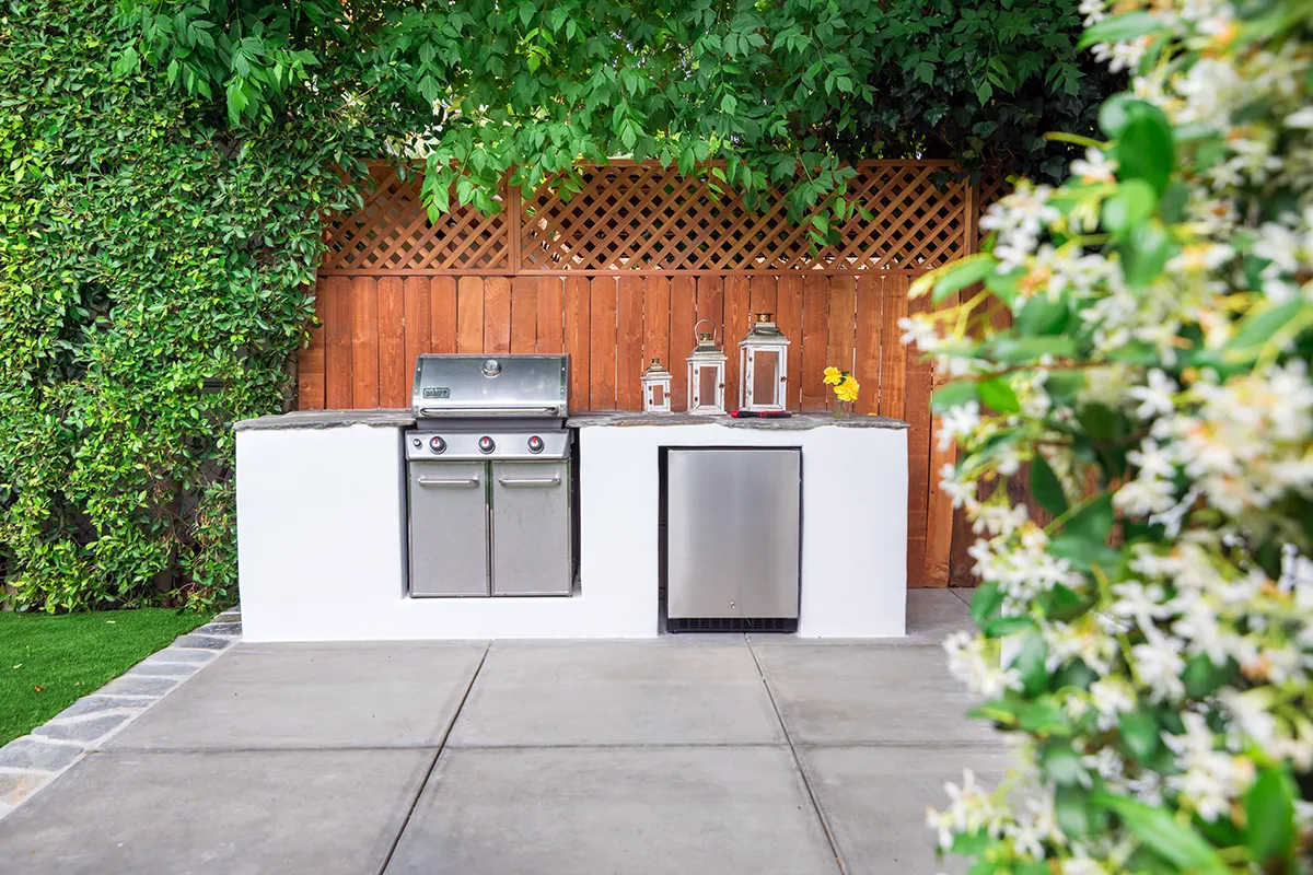 Modern outdoor kitchen with built-in stainless steel grill, concrete countertops, integrated storage, and concrete patio installation