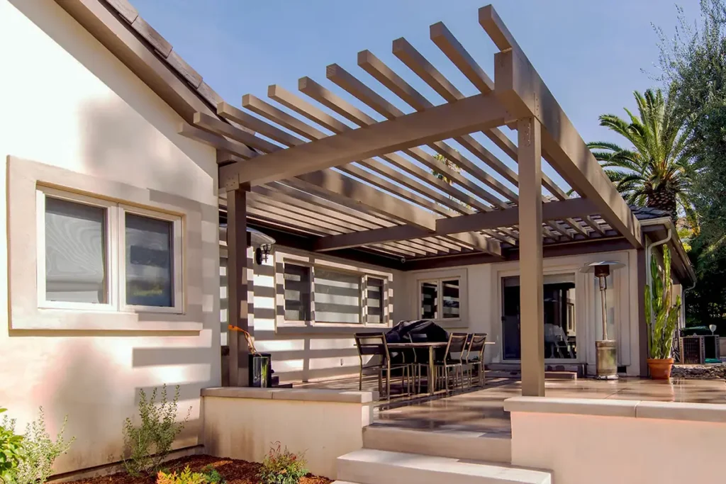 Modern pergola structure providing shade over a covered outdoor patio with dining area and concrete steps.