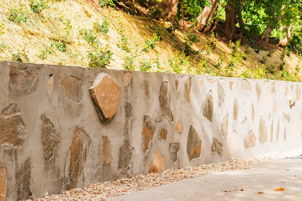 Concrete retaining wall with decorative flagstone facing and gravel edging along a hillside landscape in Hollywood Hills, Los Angeles, CA