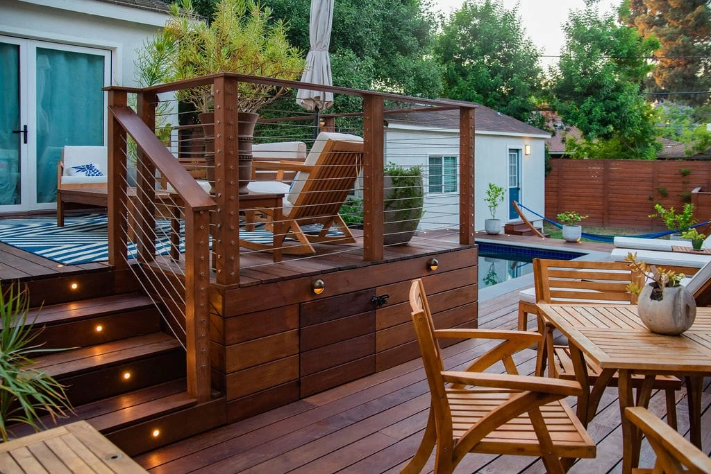 Multi-level IPE wood deck with cable railing, integrated deck lighting, wall sconces, under-deck storage, and poolside seating in Studio City, California