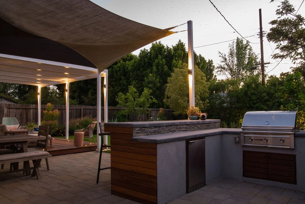 Outdoor kitchen with interlocking pavers, IPE deck, louvered patio cover, and outdoor lighting in Sherman Oaks CA