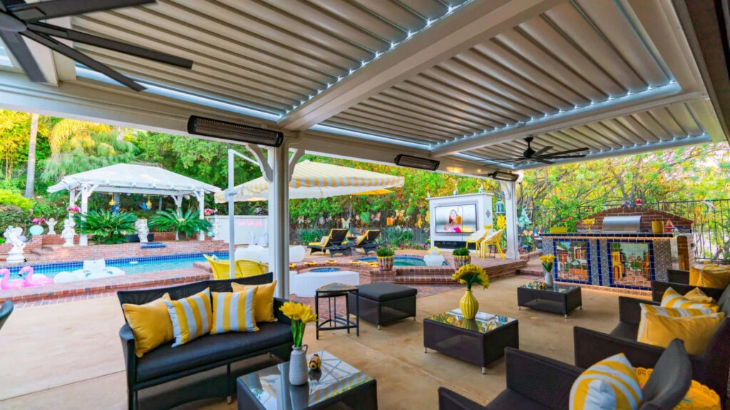 Covered outdoor living area with louvered motorized patio cover, outdoor heaters, ceiling fan, custom BBQ island, and outdoor TV structure in Encino, CA