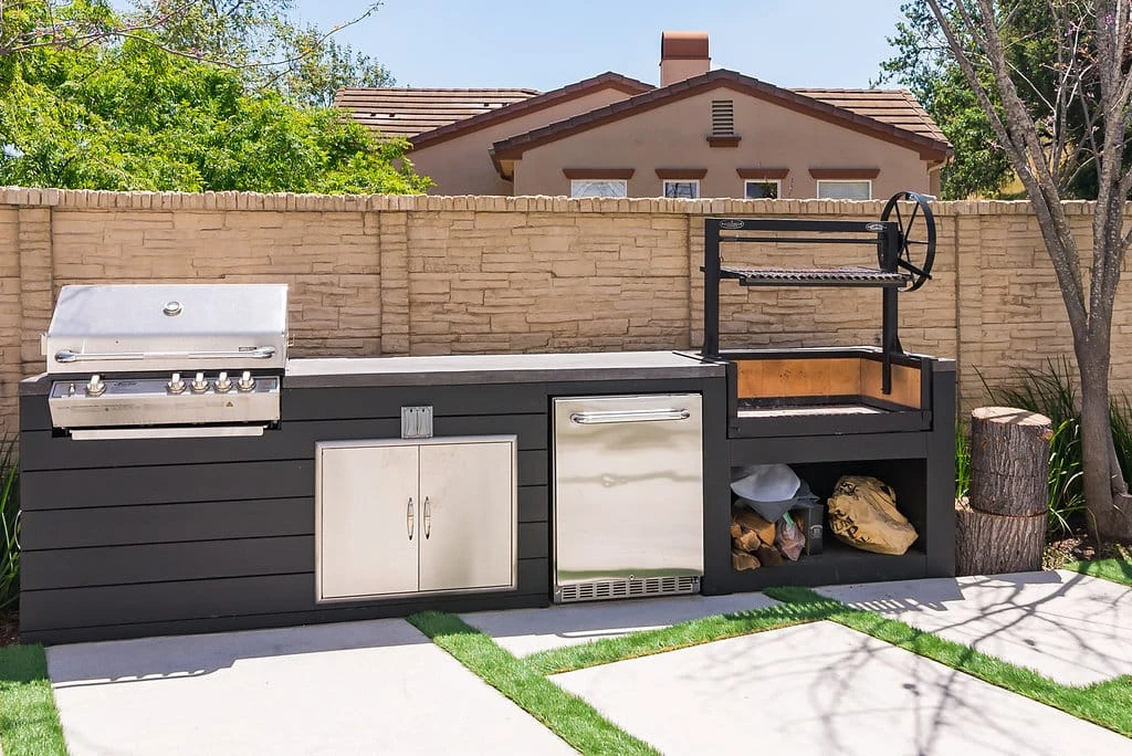 Custom outdoor kitchen with Argentine grill, gas BBQ, built-in storage, and concrete patio with turf joints in Westlake Village, CA