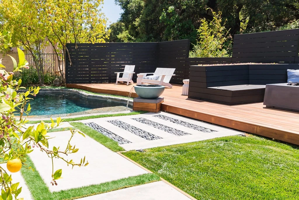 Raised pool deck with IPE wood decking, horizontal redwood guardrail stained black, custom water feature bowl, concrete pads with Mexican beach pebbles, and turf lawn in Westlake Village, CA