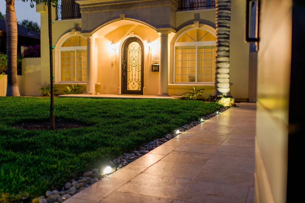 Travertine entry walkway with recessed landscape lighting, river rock edging, and Saint Augustine sod lawn in Los Angeles CA