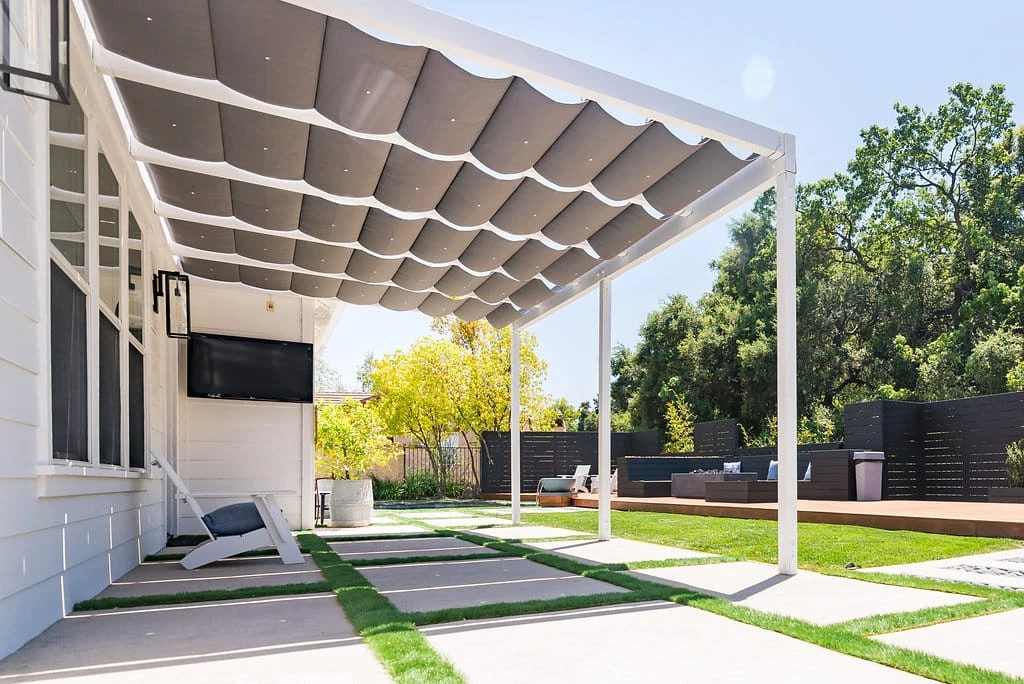 Custom patio cover with retractable shade, outdoor TV entertainment area, concrete patio with turf joints, and lawn with sprinkler irrigation in Westlake Village, CA