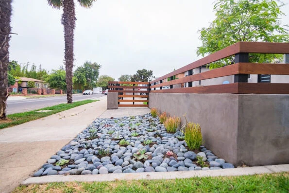 Stucco finish block wall with horizontal IPE wood fence, black river pebbles, and succulent planting along a Los Angeles front yard sidewalk