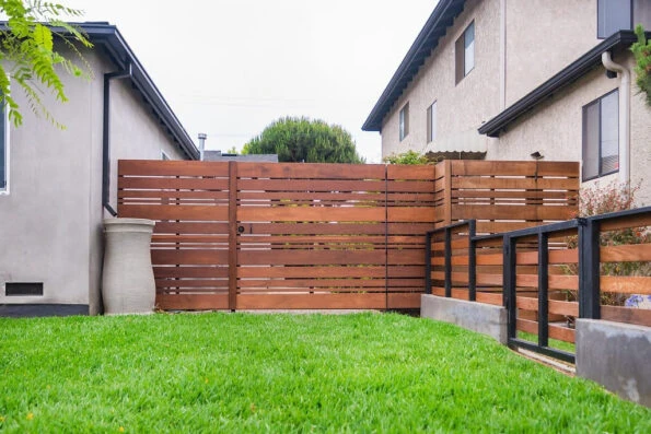 Side yard view of a horizontal IPE wood fence and gate with metal framing, Saint Augustine sod, and modern residential landscaping in Los Angeles